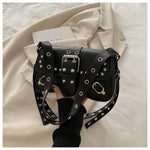 Black handbag with silver studs held by a person on a beige fabric background