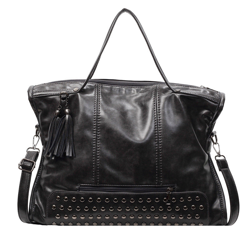 Black leather handbag with studded detail and tassel on a white background