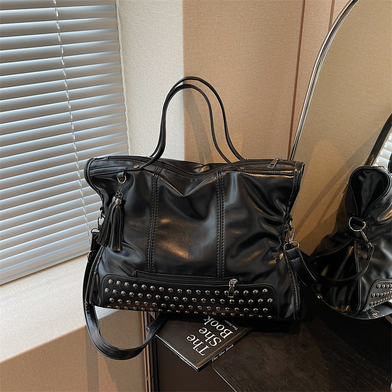 Black leather handbag with studs on a surface next to a book