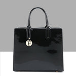 Black patent leather handbag with a gold charm on a gray background