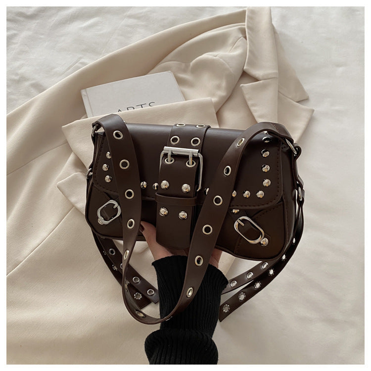 Brown leather handbag with studs held by a person on a light background