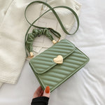 Green quilted handbag with a heart-shaped clasp on a light background