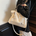 Person holding a beige handbag with studded details indoors.
