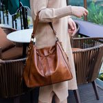 Person holding a brown leather handbag outdoors
