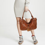 Person holding a brown leather handbag with a tassel