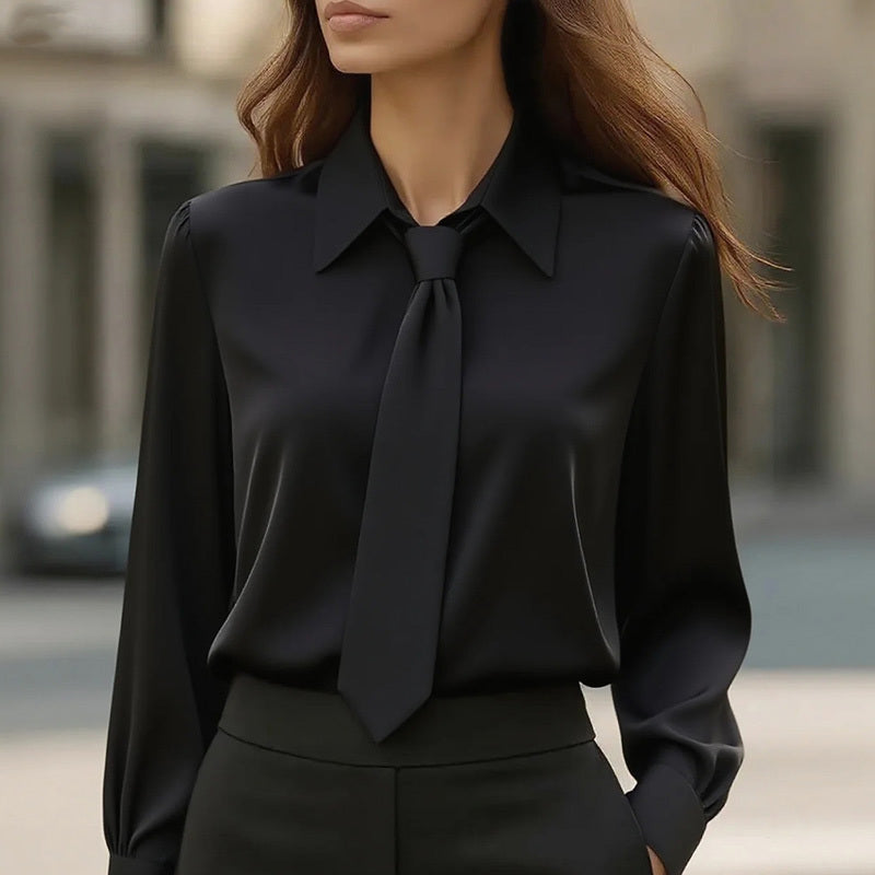 Person wearing a black blouse with a tie and black pants outdoors.