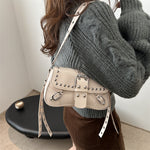 Person wearing a gray sweater with a beige studded handbag.