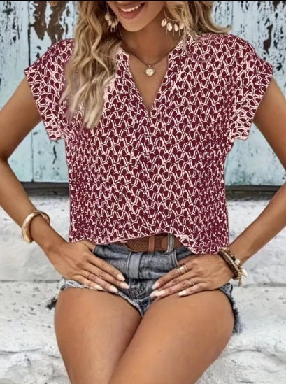 Woman wearing a patterned top and denim shorts sitting on a wooden floor.
