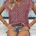Woman wearing a patterned top and denim shorts sitting on a wooden floor.